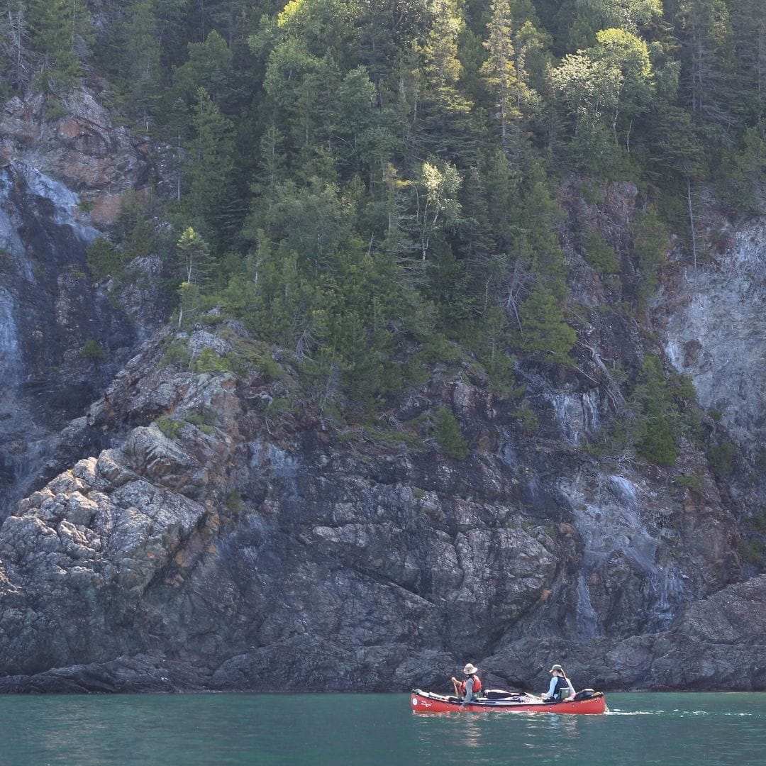 Canot double rouge avec toile de pontage navigant sur les eaux turquoises d'un lac